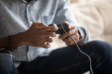 Close up image African fellow sitting on couch holding joypad playing playstation games at home. Concept of person addicted with videogames, spend free time using modern gadgets digital entertainment © fizkes