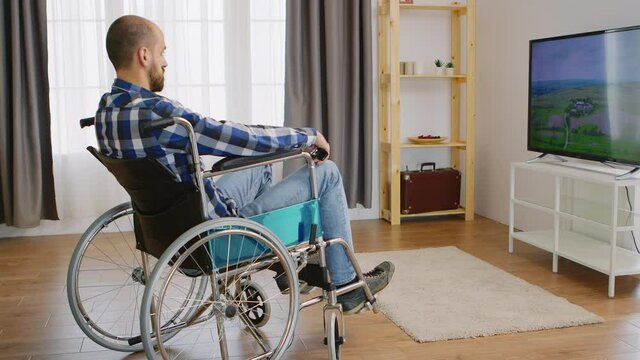 Paralyzed and depressed young man in wheelchair watching tv. Handicapped invalid paralysed person, alone at home, depression and health problems, pensive, sad and unhappy man