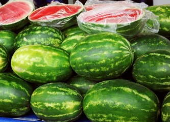 Large pile of green striped watermelons, a market bench for a watermelon merchant, cut red watermelons lie on top. Berry. Business. Background