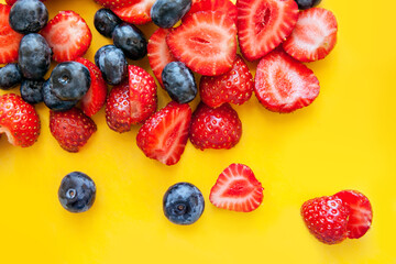 Mixed fresh berries: blueberry and strawberry on a yellow background