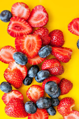 Mixed fresh berries: blueberry and strawberry on a yellow background
