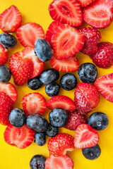 Mixed fresh berries: blueberry and strawberry on a yellow background