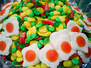 A bunch of bright colored jelly in the shape of pineapples, carrots and eggs lying on a counter in a candy store