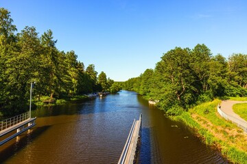 Beautiful landscape view of river with green forest trees on both sides on blue sky background.