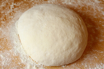 Color photo of round dough in flour on a wooden table. Appetizing cooking. Work in the kitchen.