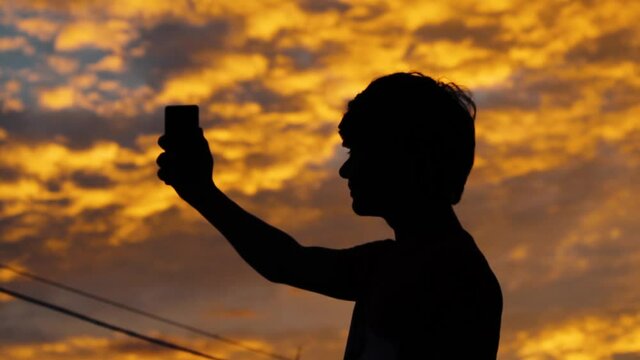 Silhouette of a kid taking selfie with mobile phone during the sunset