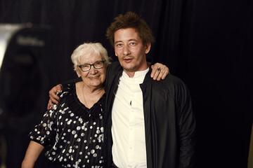 Two generations. Indoor family portrait of mature wrinkled gray haired woman dressed in stylish blouse, surrounded with love of son, enjoying time together, isolated on black studio wall. Film effect.