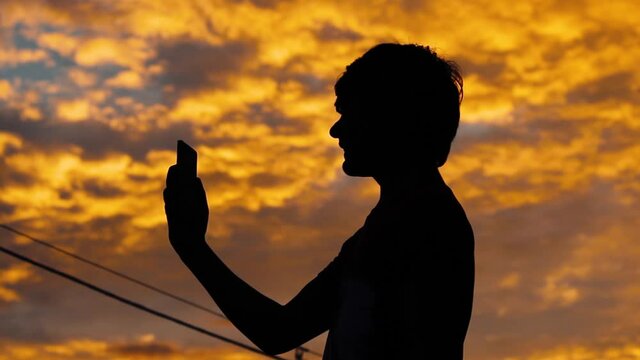Silhouette of a kid talking on mobile phone in front of sky during sunset
