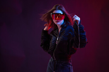 Stylish girl in glasses and jacket dancing in a nightclub in smoke on a dark background in neon light.