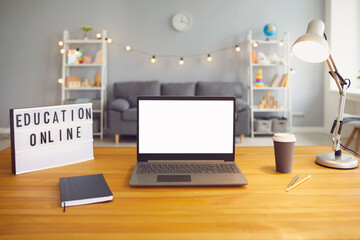 Online education sign and laptop computer with empty screen standing on wooden table in living room, mockup for design