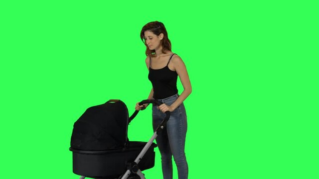 Relaxed mother pushing a stroller, smiling, and waves hello to a friend, over green screen.