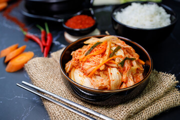 Eating kimchi cabbage and rice in a black bowl with chopsticks.