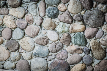 Stone wall as a background. Masonry made of natural, polished by the sea, cobblestones. Multi-colored, natural stones in the interior.