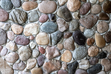 Stone wall as a background. Masonry made of natural, polished by the sea, cobblestones. Multi-colored, natural stones in the interior.