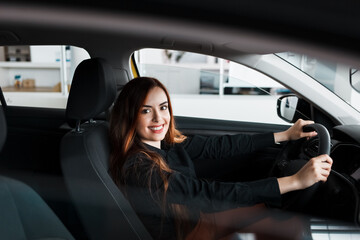 Smiling woman sitting at a car in a showroom