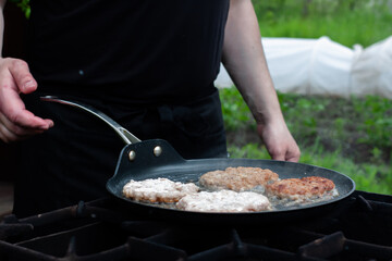 the cook roasts the cutlets in a pan over the fire. food on the grill in nature. picnic.