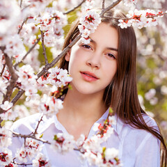 Naklejka premium Pretty teen girl are posing in garden near blossom cherry tree with white flowers