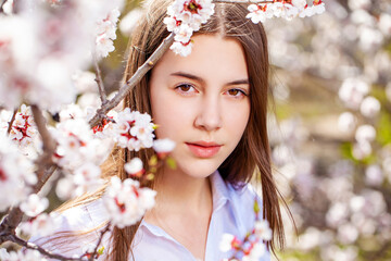 Pretty teen girl are posing in garden near blossom cherry tree with white flowers