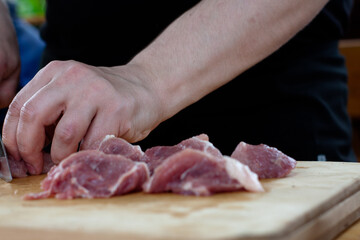cutting meat into pieces with a knife on a wooden Board. the cook cuts the meat.