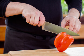 the cook slices red peppers on a wooden Board