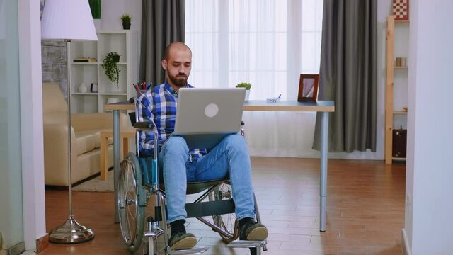 Handicapped freelancer in wheelchair working on laptop. Handicapped invalid paralysed freelancer, immobilized entrepreneur working from home, ilness and disability