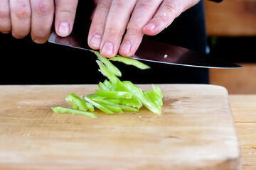 the cook cuts green peppers into strips on a wooden Board