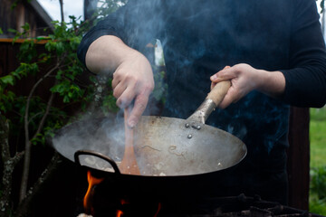 the cook mixes onions, carrots with chicken in a wok with a wooden spatula