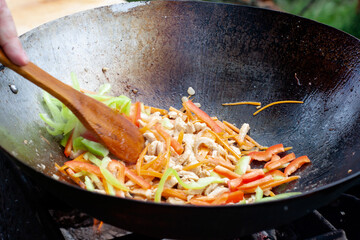 cook with a wooden spatula stir onions, carrots and chicken in a wok on the fire