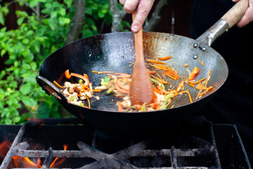 cook with a wooden spatula stir onions, carrots and chicken in a wok on the fire