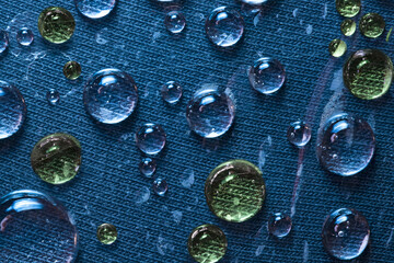 Texture. Translucent flowing blue and green raindrops are located on the blue cloth background. Close-up. 