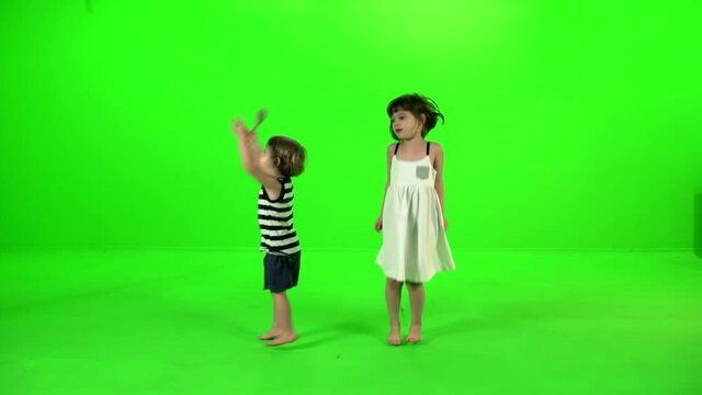 Two cute little kids dancing and playing around happily over green screen.
