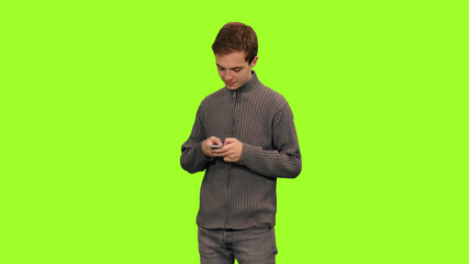 Portrait of young man student texting sms on green screen background, Chroma key, Front view
