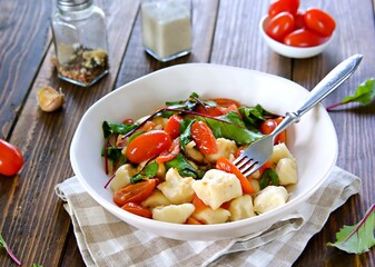 Lazy dumplings or gnocchi from cottage cheese with toppings of stewed tomatoes and young beet tops