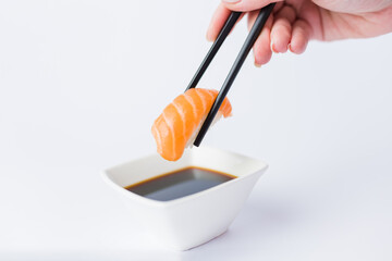 Close up of woman holding chopsticks with salmon sushi roll and bowl with soy sauce on table, japanese traditional healthy meal concept.
