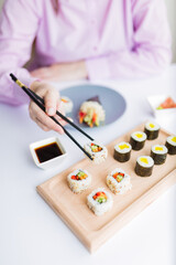 Obraz na płótnie Canvas Close up of female eating sushi portion roll with chopsticks at restaurant.