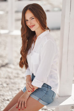 Pretty woman on the beach at summer white shirt and denim shorts wooden background sitting 