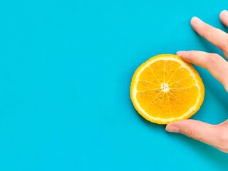 bright juicy sliced orange on a hand isolated on blue background