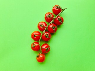 A branch of red cherry tomatoes on a green background. Small and juicy vegetable is rich in vitamins and trace elements. Healthy food. Fresh and organic vegetables. Raw food. Top view with copy space.