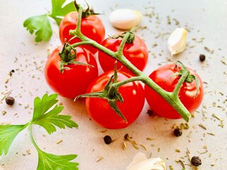 Fresh red cherry tomatos, spices, pepper, garlic, parsley, herb on gray background
