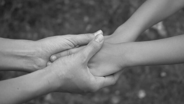Closeup view black and white video footage of hands of mother and little son holding hands together, mom touching sking of her baby with love and tenderness.