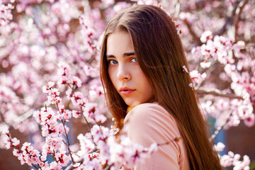 Fototapeta premium Young girl posing near blossom cherry tree with pink flowers