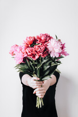 Faceless girl holds a bouquet of peonies on concrete wall background. Incognito flower delivery....