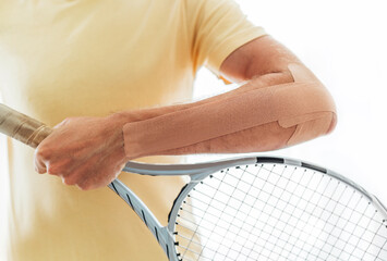 Tennis player elbow taped with elastic therapeutic or Kinesio tape applied on arm lying on racket...