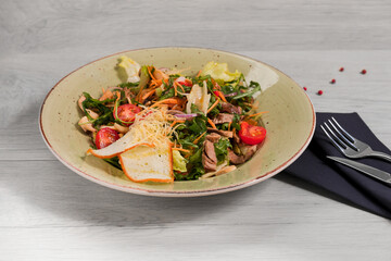 The plate with salad with roast beef (ingredients: baked peppers, tomatoes, pickled onions, a mix of fresh herbs and breadcrumbs) on a light gray background.