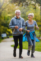 Smiling senior couple jogging in the park - obrazy, fototapety, plakaty