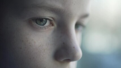 Close-up plan of the child sad eyes. The depressed boy loking through the window.