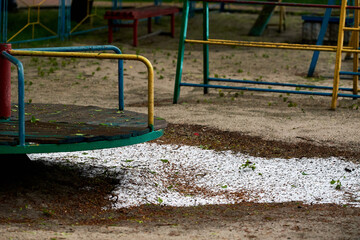 A hill of hail lay on the sand in the playground in the spring. bad weather. there are no people.