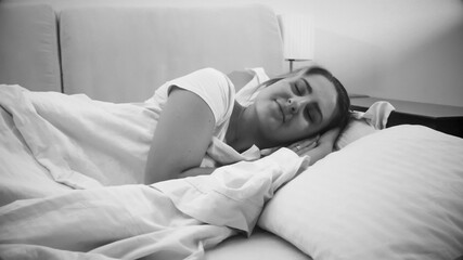 Black and white portrait of smiling young woman sleeping in bed at night