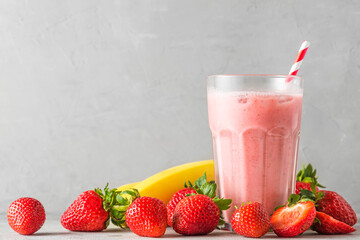 Strawberry and banana smoothie or milkshake in a glass with a straw with fresh fruits. refreshing...