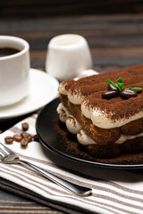 Classic tiramisu dessert on ceramic plate, milk or cream and cup of coffee on wooden background